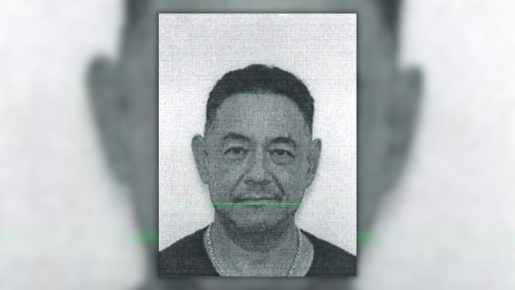 Grainy black-and-white photo of Sam Martin Chambers, a man with short dark hair wearing a dark shirt and a chain necklace.